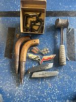 Full lot overview showing car badges, garden tools, C clamps, lead hammer, and utility cutters on a blue background