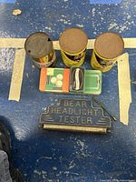 Overview photo of two automatic transmission fluid cans, one empty motor oil can, glass cutter, and Bear Headlight Tester metal sign