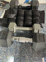 Three pairs of hex dumbbells (5, 10, 15 lb) and four black adjustable wrist or ankle weights on carpeted floor.