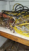 Multiple indoor and outdoor extension cords coiled on a wood shelf, showing various lengths and colors including yellow, brown, and black cords.