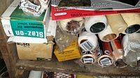 Image showing a variety of paint roller sleeves, some still in packaging, displayed on a wooden surface along with boxes and partial items nearby.