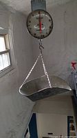 Vintage Hanson hanging produce scale with large metal tray and dial gauge, hanging indoors in rustic setting.
