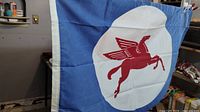 Full view of the flag hanging showing blue background with central white circle and red Pegasus horse.