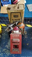 Front view of the rectangular All Weather SAE 10W-30 motor oil can with several other oil cans and the vintage red Cardox fire call box in the foreground.