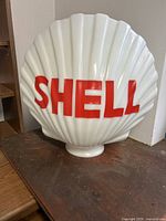 Front view of white scallop-shell shaped glass globe with red SHELL letters
