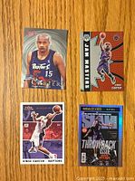 Front view of four Vince Carter basketball cards placed on a wooden surface: including a Topps Stadium Club rookie card, Panini Jam Masters, Fleer, and NBA Hoops Throwback Issue cards.