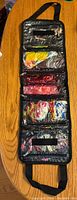 Top view of black fabric carrying case laid flat showing five clear zippered compartments filled with multiple packs of colorful soft plastic Berkeley Power Baits.