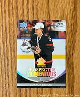 Front of the Connor Bedard hockey card showing him in Team Canada black jersey holding a trophy with holographic gold maple leaf and text.