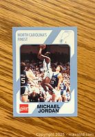 Front of Michael Jordan basketball card showing player in North Carolina uniform making a shot with crowd background and card branding.