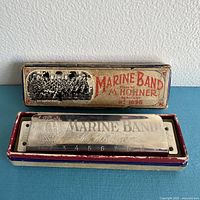 Antique Marine Band harmonica resting on its original vintage box with a graphic of a band printed on the box cover.
