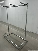 Full view of vintage metal clothing rack with curved base and three hanging bars.