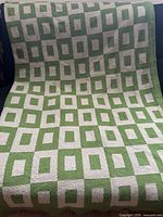 Full view of the blanket displayed on sofa showing the green and taupe geometric square pattern covering the entire surface.