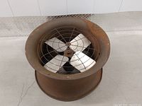Top view showing four metal fan blades and protective wire grille inside rusted metal housing.