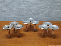 Front view of 9 stackable vintage silver-tone candle holders arranged in groups on a wooden surface.
