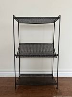 Full front view of the metal shelf unit showing three shelves with lattice metal design and ball feet.