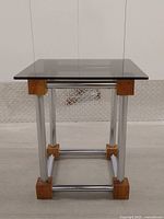 Side angle showing overall cube design with chrome tubular frame and wooden corner blocks supporting glass top