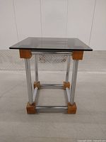 Front view of the cube end table showing glass top and chrome steel legs with wood blocks.