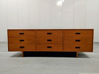 Front view of dresser showing nine drawers and black rectangular recessed pulls on teak body