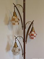 Close-up of three checkered glass shades and scroll brass-tone arms on central pole