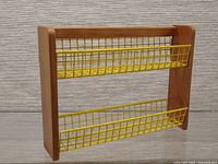 Front view of the vintage wall-mounted spice jar rack showing the wooden frame and two yellow rubberized wire baskets for storage.