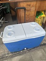 Blue and white Igloo cooler showing exterior top with four cup holders and retractable handle for transport.