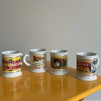 Four vintage shaving mugs arranged in a row showing full designs and handles.