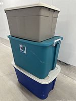 Three stacked large storage totes showing different colored bases and matching beige lids. The totes are clean but used.