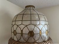 Image showing full view of vintage Capiz lampshade with metal goldtone framing. Slightly rounded shape with geometric pattern panels.