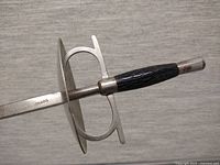 Close-up of fencing foil handle with guard and grip, showing the 'Toledo' mark on the blade.