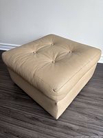 Front and side view of taupe leather ottoman showing full shape and tufting