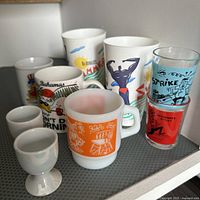 Assorted mugs, egg cups, and shot glasses with colorful graphic designs seen together on a shelf