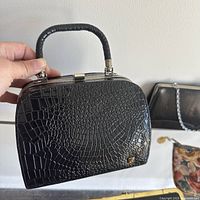 Black vintage handbag with faux crocodile embossing and top handle showing wear to frame.