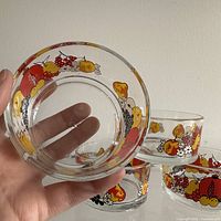 Closeup of the bottom of one glass Pyrex bowl held by hand showing the vintage fruit motif decoration around the rim.