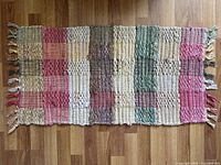 Top view of the rectangular vintage rag rug showing its pastel colored checkered pattern with tassels on ends.