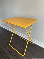 Yellow metal folding table angled view showing top surface and foldable tubular legs.
