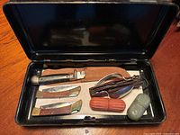 Full open black metal case displaying all items inside: four pocket knives, utensil kit, green Cutter Snake Kit case, and orange Snake Bite Kit case.