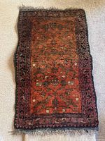 Dark red and black traditional patterned rectangular floor rug with fringed edges, displayed on carpeted floor.