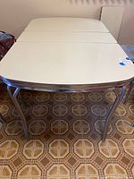 Front view of rectangular beige laminate top table with chrome trim and tubular chrome legs on patterned floor.