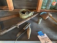 Overview photo showing all six items arranged on a shelf: bayonet with scabbard, metal knife, twine spool, metal container, belt, and axe with sheath.