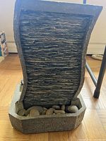 Front view showing textured curved water panel with decorative rocks in the basin.