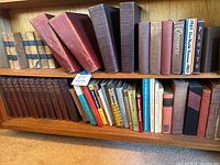 Wide view of multiple shelves with a collection of vintage and contemporary books, many leatherbound, including large Thick red and brown volumes.