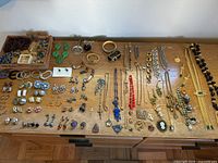 Top-down photo showing a large vintage jewelry selection arranged on a wooden dresser with necklaces, bracelets, rings, earrings, and brooches.