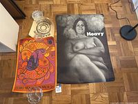 All three vintage posters laid out on a parquet floor: Heavy (737) poster showing a nude woman on the right, colorful Pisces zodiac poster in the middle, and Zzzoom Donuts poster on top left.