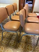 Front and side view of six salmon vinyl mid-century diner chairs with chrome legs, showing overall set condition and alignment.
