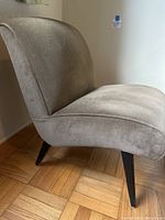 Side view of vintage slipper chair showing curved backrest and black tapered wooden legs on parquet floor.