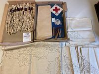 Photo showing beige linen napkins with printed embroidery floral templates and skeins of ecru cotton floss in a box, plus needles and a war fund sticker.