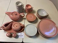 Overall set layout with pink and gray glazed ceramic dishes including plates, cups, saucers, and serving pieces on white table.