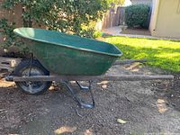 Side view of green wheelbarrow showing metal bin, wooden handles, and tire.