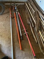 Wide view showing the Ridgid oversized metal landscape rake and four pole tools including branch cutters and fruit picker tools with orange to red handles and cords.