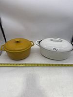 Two cast iron pots side by side, one white oval pot and one yellow round pot, each with lids
